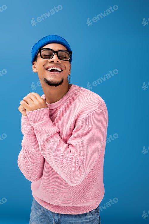 Preview: Charming young man exuding confidence in vibrant pink sweater and blue beanie