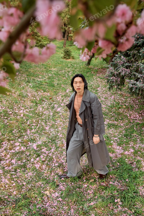 Preview: Stylish young man in grey outfit enjoying a serene day in a blooming park