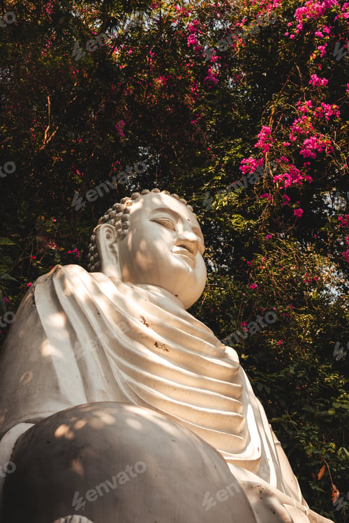 Preview: White Buddha statue among lush greenery and colorful flowers in a serene park setting