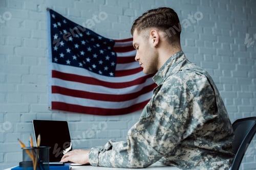 Preview: low angle view of handsome soldier using laptop with blank screen