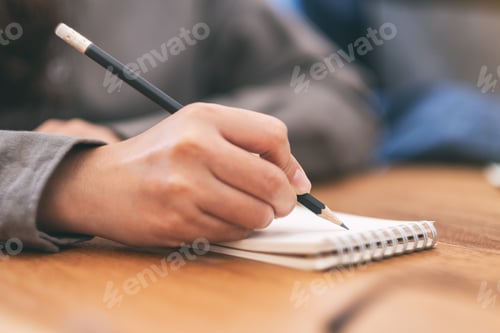 Preview: Closeup image of a woman's hand writing on blank notebook on wooden table