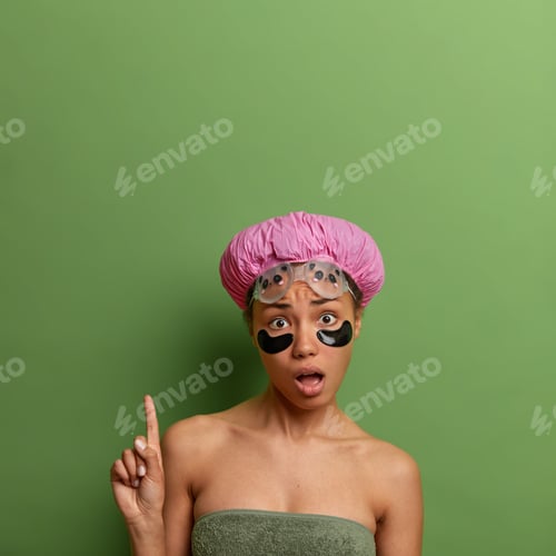 Preview: Vertical shot of surprised young woman points fore finger above, has beauty and hygiene procedures a