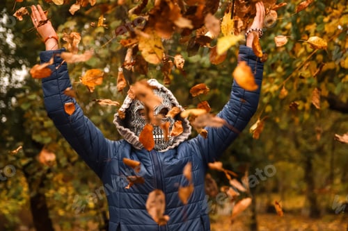 Preview: Halloween people. Person in grim reaper mask raising hand and throwing leaves. Many flying orange, y