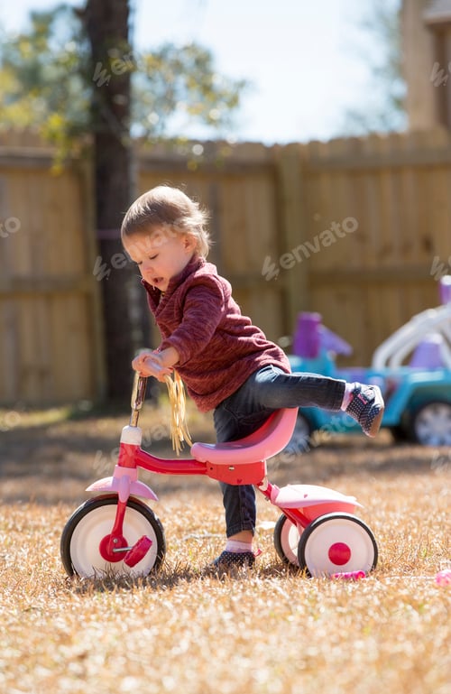 Preview: Female toddler playing on tricycle in garden