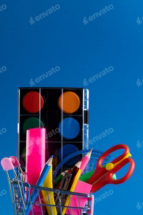 Visualização: Vista de perto do carrinho de compras em miniatura com materiais escolares e espaço de cópia em fundo azul