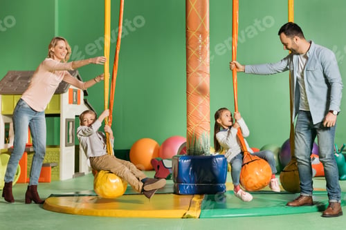 Preview: happy parents looking at kids swinging on swings in entertainment center