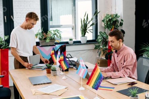 Preview: Happy couple organizing documents in a vibrant office space filled with pride flags