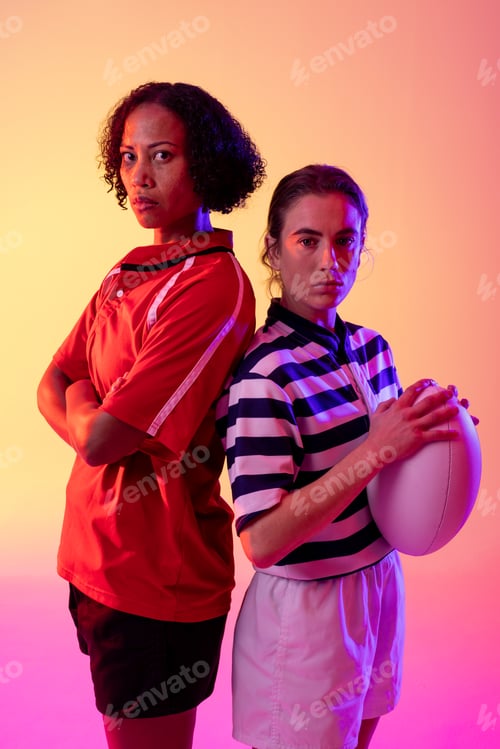 Preview: Portrait of two diverse female rugby players with rugby ball over neon pink lighting