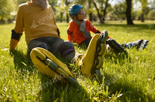 Preview: Happy man and boy rollerskaters rest on grass filed in park
