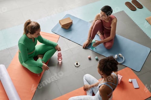 Preview: Female Yoga Instructor Sitting on Floor with Group of Women in Yoga Studio