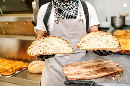 Preview: baker showing the crumb of a loaf of wheat bread with his hands and protected by black gloves