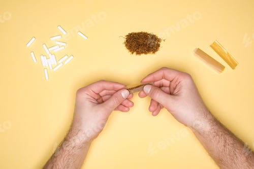 Preview: Cropped view of man making a cigarette isolated on yellow