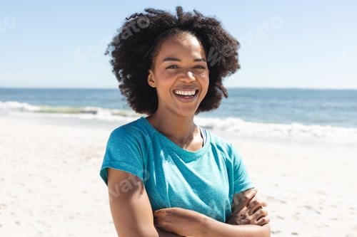 Preview: Portrait of happy african american woman looking at camera and smiling on sunny beach