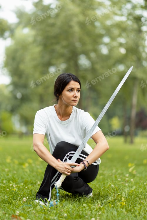 Preview: Caucasian woman working out with Tai Chi sword in the morning at the park