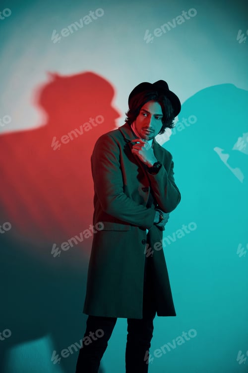 Preview: Portrait of young stylish man in hat, suit and tie that stands in neon lights in the studio