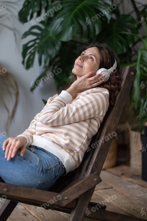 Preview: Serene woman in earphones rest in greenhouse relax listen to audiobook in surround green plants.