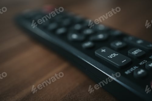 Preview: Closeup shot of a black portable remote control on a wooden table, volume button