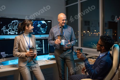 Preview: Three happy colleagues with drinks chatting at break by workplace