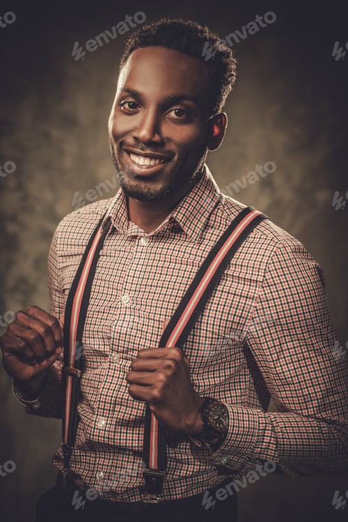 Preview: Stylish young black man with suspenders posing on dark background.