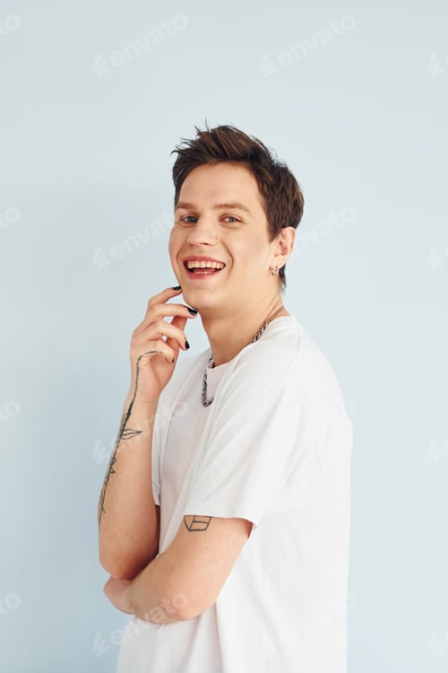 Preview: Young gay man is standing in the studio and posing for a camera. In casual white shirt