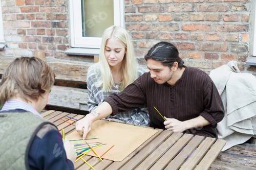 Preview: Friends enjoying a casual game of pickup sticks on a rustic outdoor table.