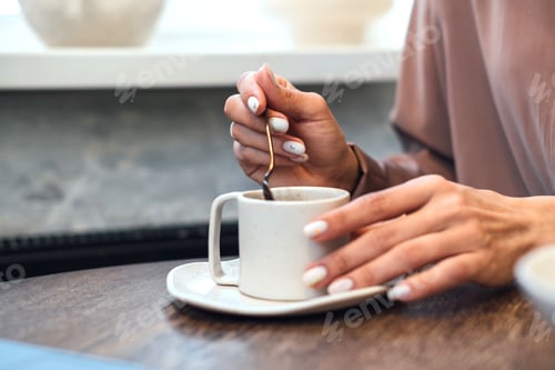 Preview: Beautiful female hands stir a gilded coffee spoon in a white mug
