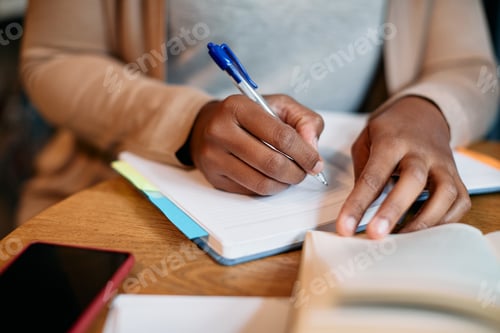 Preview: Close-up of black female student writing in notebook while learning in library,
