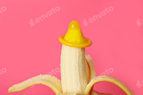 Preview: Banana with condom on pink background, close up
