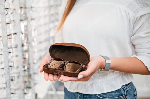 Preview: In brown colored case. Woman holding glasses in hands in the store. Close up view