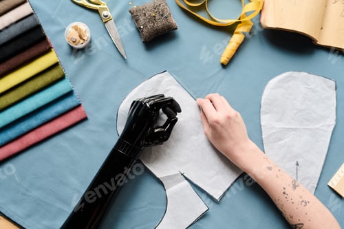 Preview: Above view of hands of female with partial arm making paper patterns of clothes