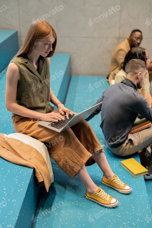 Preview: Pretty student typing o laptop keypad while sitting on blue staircase