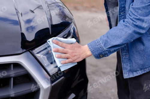 Preview: Male hand cleaning the headlights of a black car with a rag.