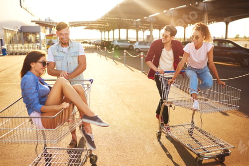 Preview: Group of happy young people having fun on shopping trolleys. Young people racing on shopping cart.