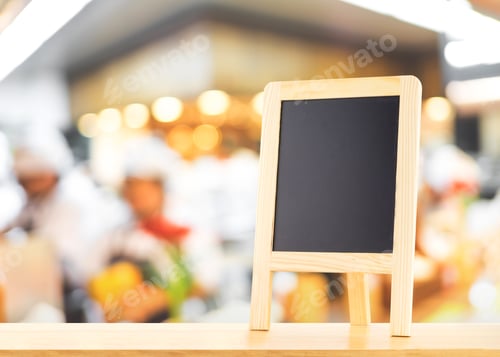 Preview: Blackboard with easel (menu board) on wooden table with blur bokeh chef counter at restaurant