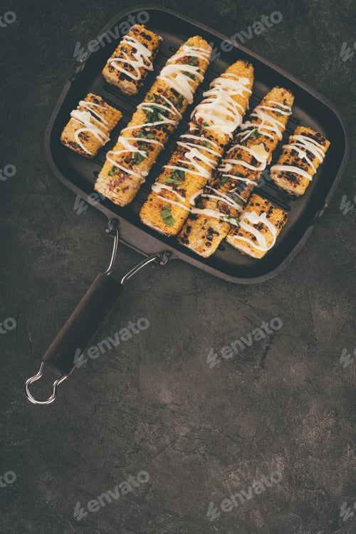 Preview: top view of frying pan with delicious grilled corncobs on black concrete table