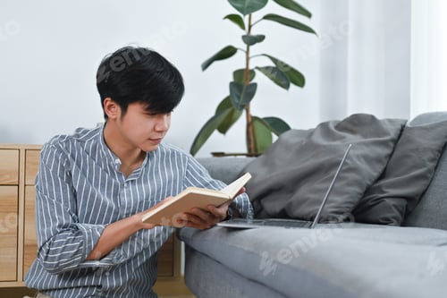 Preview: Young Man Reading a Book Indoors on Sofa