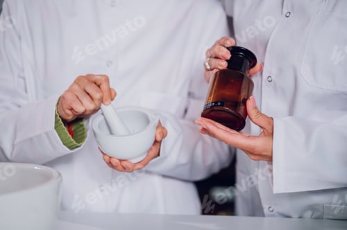 Preview: Pharmacists' hands mixing medicine in a mortar and holding a flask.