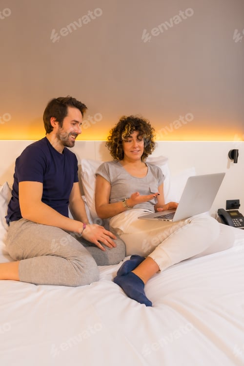 Preview: A couple in pajamas on the bed looking at an online reservation on the computer