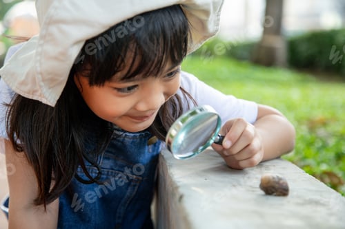 Preview: Happy kid girl exploring nature with a magnifying glass and a snail. He having fun in the garden.