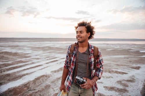 Preview: Happy man with backpack and vintage camera walking on beach