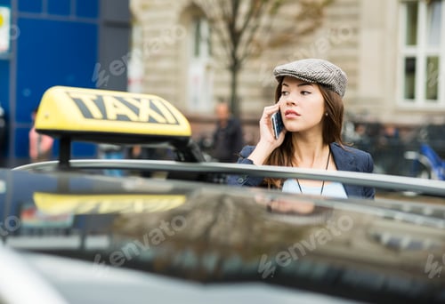 Preview: Young woman telephoning with smartphone standing behind taxi