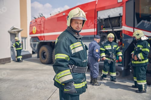 Preview: Team of happy firefighters learning on trucks at fire station
