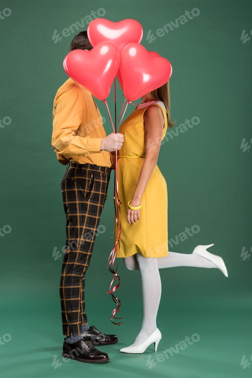 Preview: couple covering faces with heart shaped balloons on green background