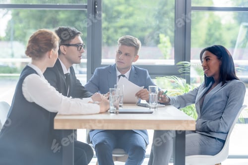 Preview: Behind the glass view of concentrated business people discussing project in modern office