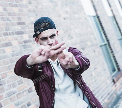Preview: Portrait of young man gesturing in front of brick wall