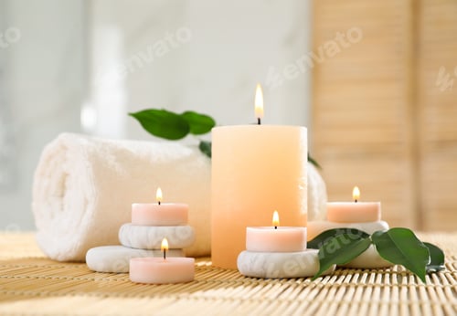 Preview: Composition of spa stones, towel and burning candles on bamboo mat