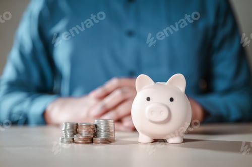 Preview: A person sits with a piggy bank full of coins on a table. The coins