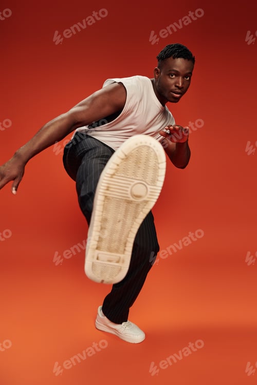 Preview: hot african american guy in striking pose with outstretched leg on red and orange backdrop
