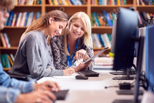 Preview: Female University Or College Student Working At Computer In Library Being Helped By Tutor