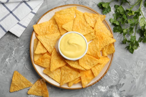 Preview: Tasty cheese dipping sauce in bowl, nacho chips and parsley on grey table, flat lay
